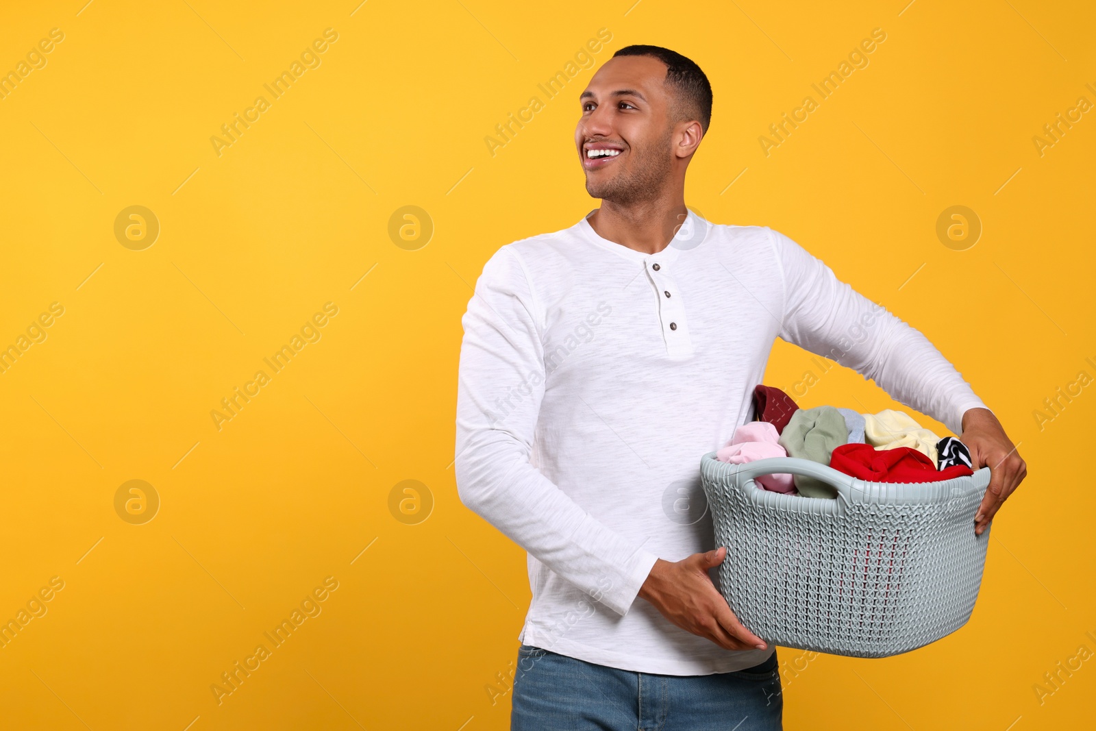 Photo of Happy man with basket full of laundry on orange background. Space for text