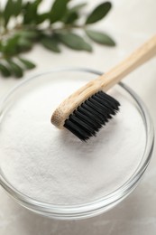 Photo of Bamboo toothbrush and glass bowl of baking soda on light table, closeup