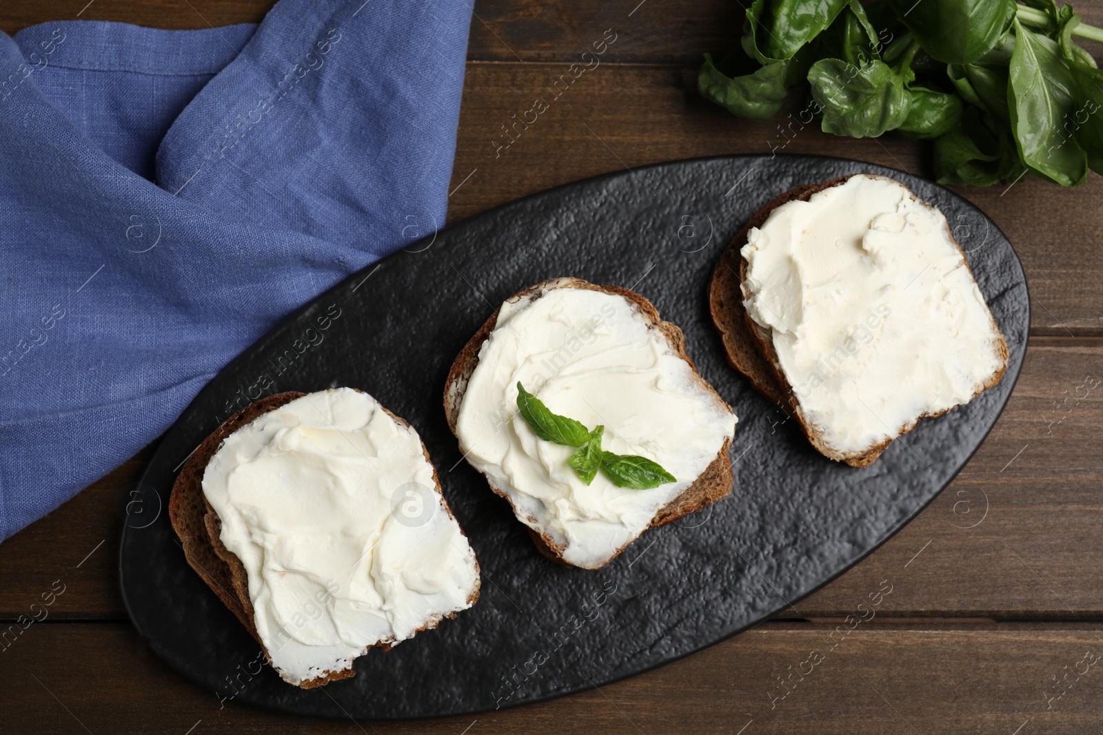 Photo of Bread with cream cheese on wooden table, flat lay
