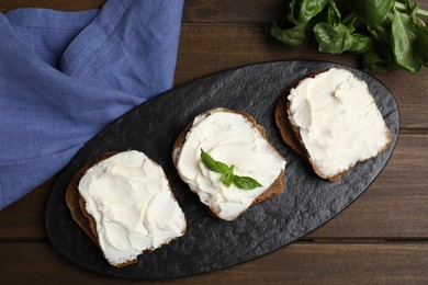 Bread with cream cheese on wooden table, flat lay