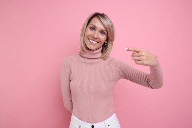 Beautiful happy woman pointing on pink background