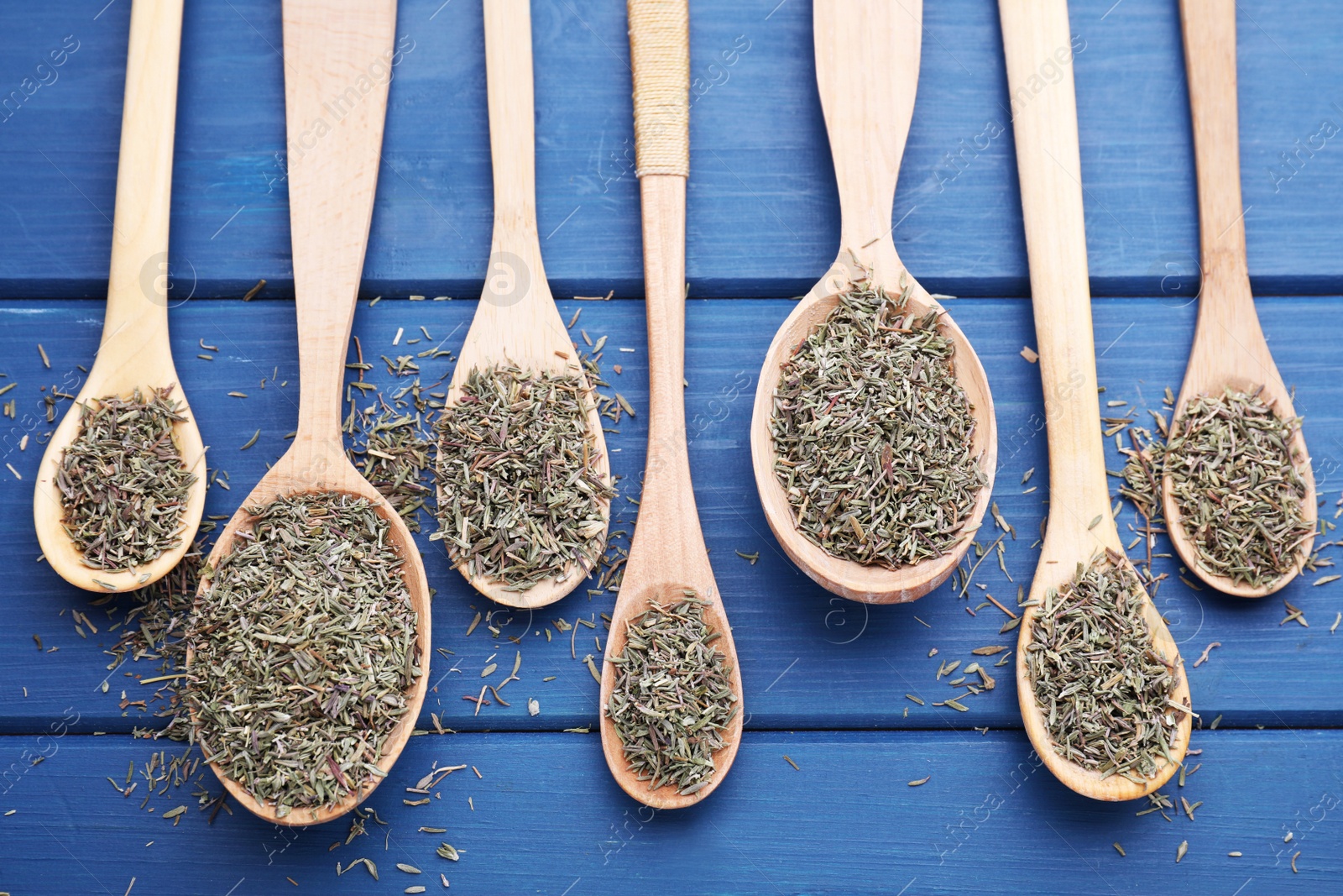 Photo of Spoons with dried thyme on blue wooden table, flat lay