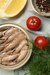 Tin can with tasty sprats served on table, flat lay