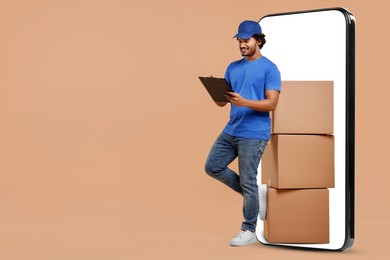 Image of Courier with stack of parcels and clipboard near huge smartphone on dark beige background. Delivery service. Space for text