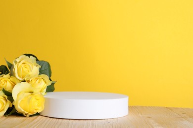 Photo of Beautiful presentation for product. White round podium and roses on wooden table against yellow background, space for text