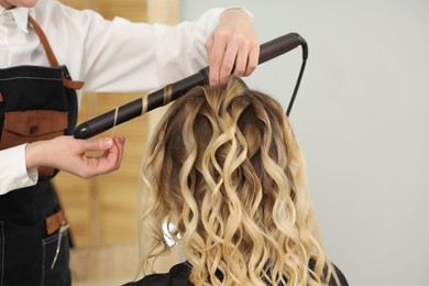 Photo of Hair styling. Hairdresser curling woman's hair in salon, closeup