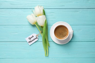 White tulips, coffee and tag with text Good Morning on light blue wooden table, flat lay