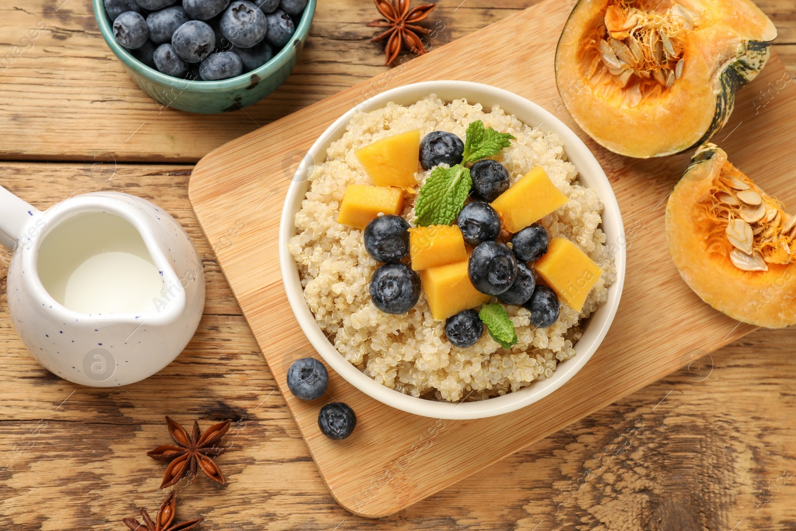 Photo of Flat lay composition with bowl of tasty quinoa porridge, blueberries and pumpkin on wooden table