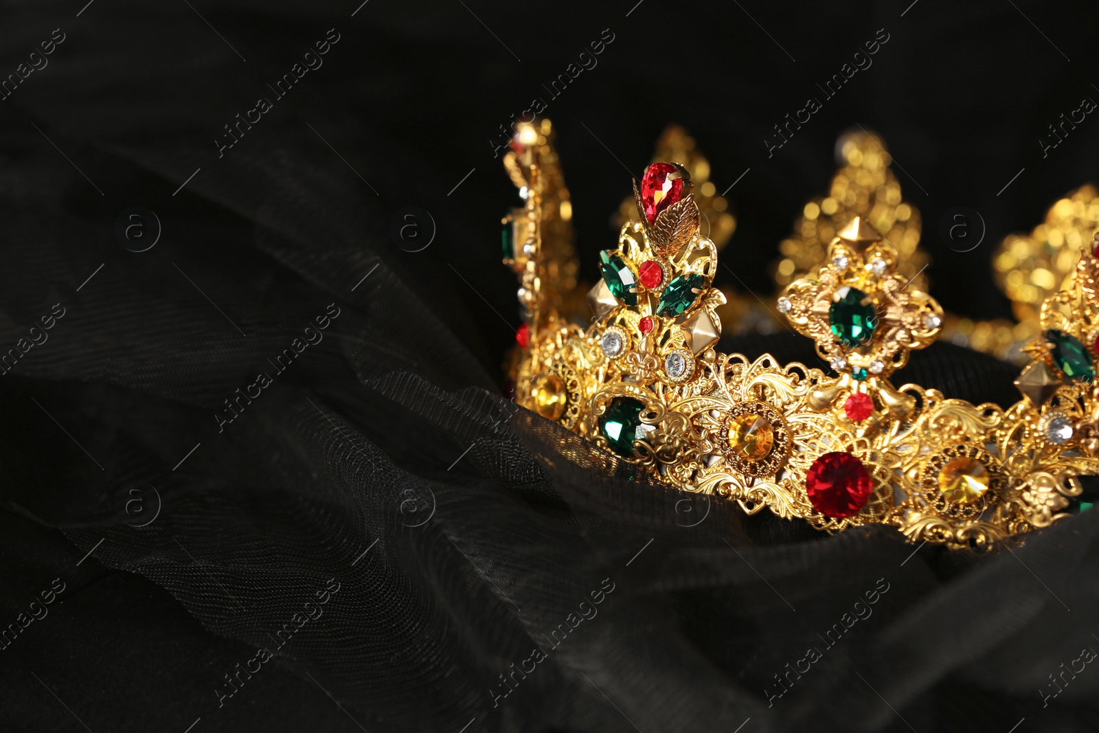 Photo of Beautiful golden crown with gems on black cloth, closeup. Space for text