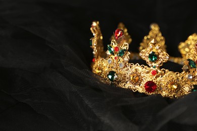 Beautiful golden crown with gems on black cloth, closeup. Space for text