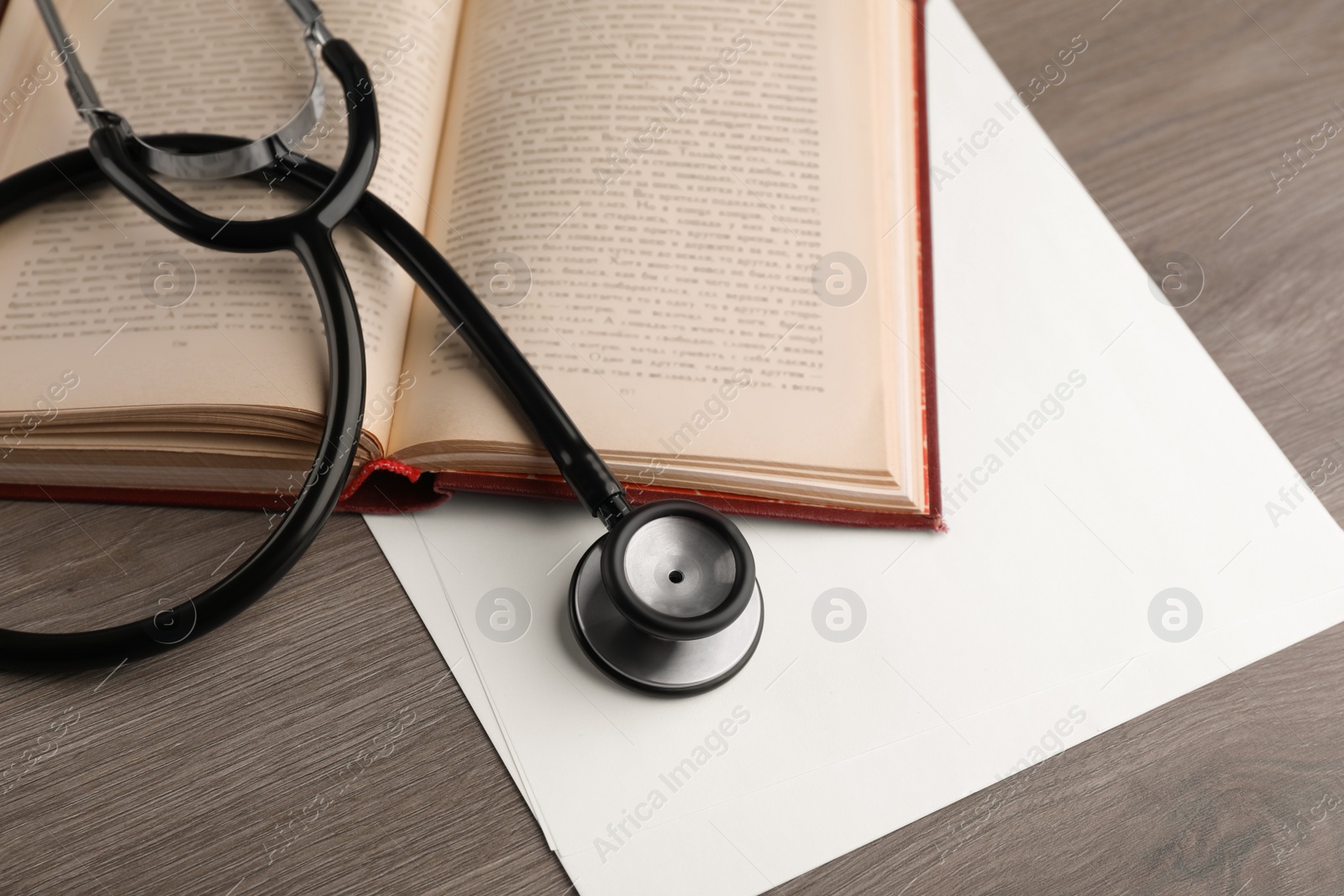 Photo of Book, stethoscope and sheets of paper on wooden table, above view. Medical education