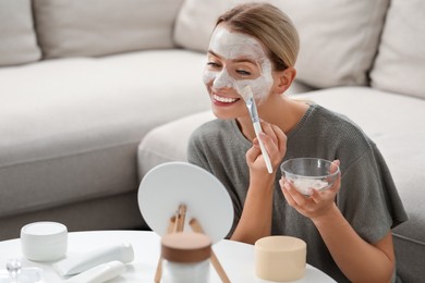 Photo of Young woman applying face mask in front of mirror at home, space for text. Spa treatments