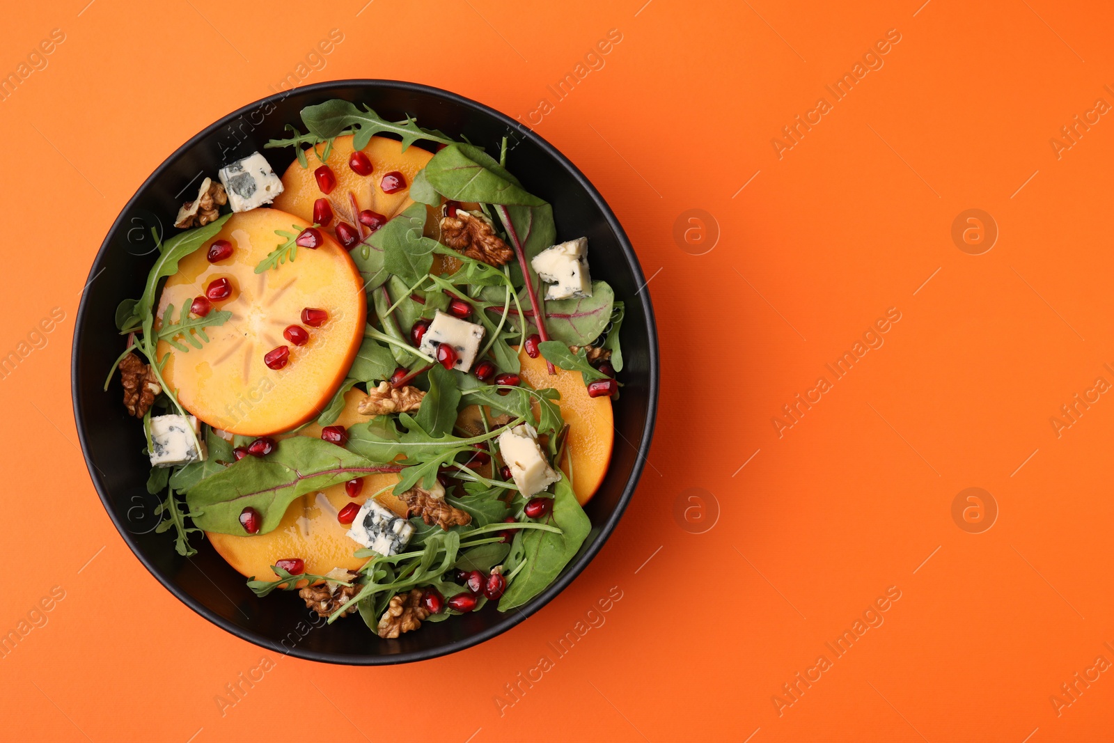 Photo of Tasty salad with persimmon, blue cheese, pomegranate and walnuts on orange background top view. Space for text