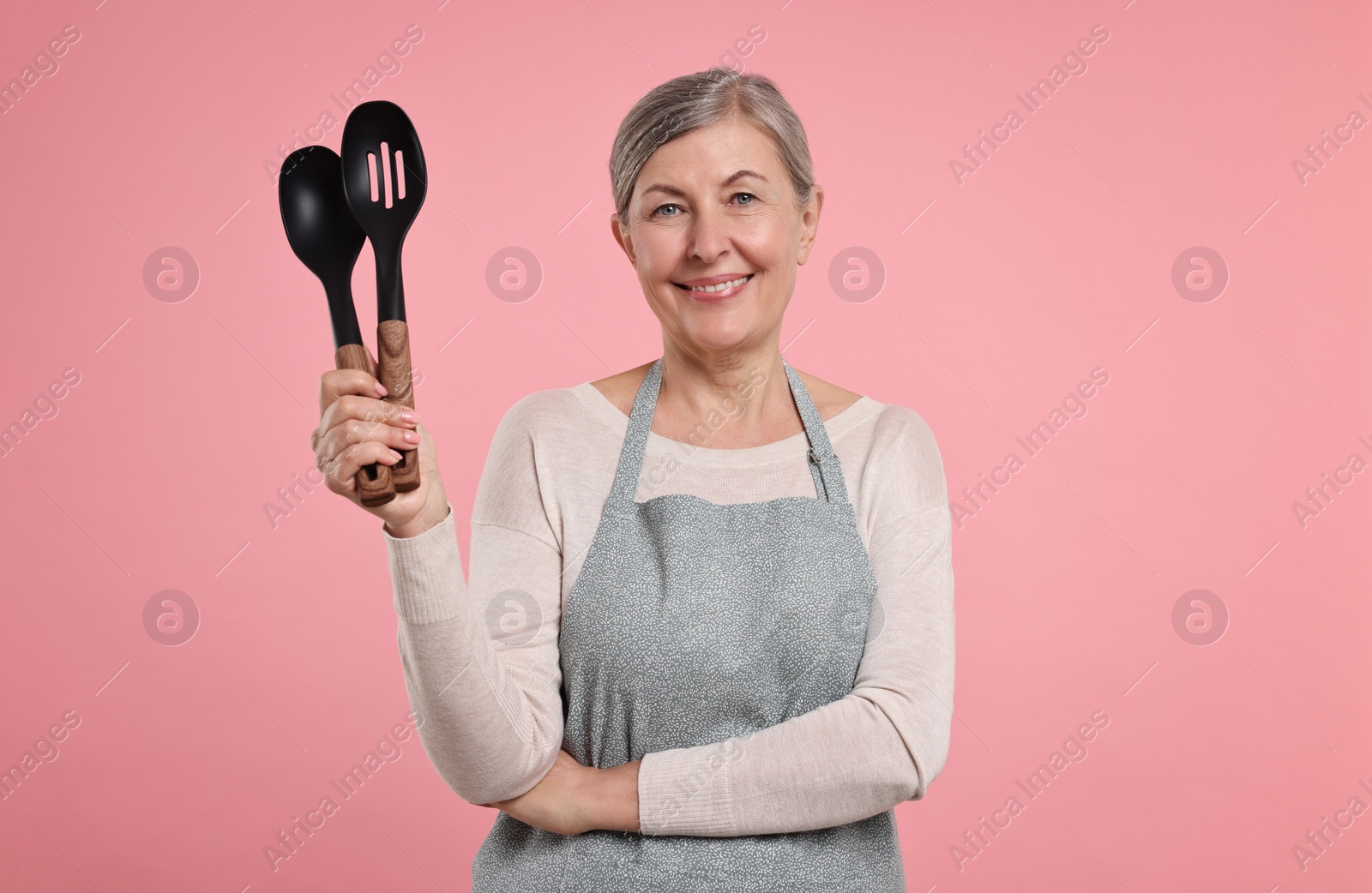 Photo of Happy housewife with spoons on pink background