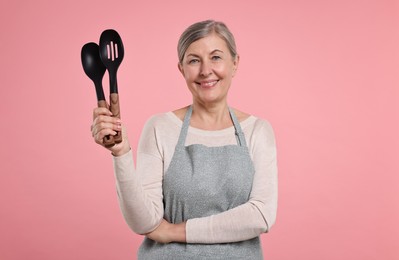 Happy housewife with spoons on pink background