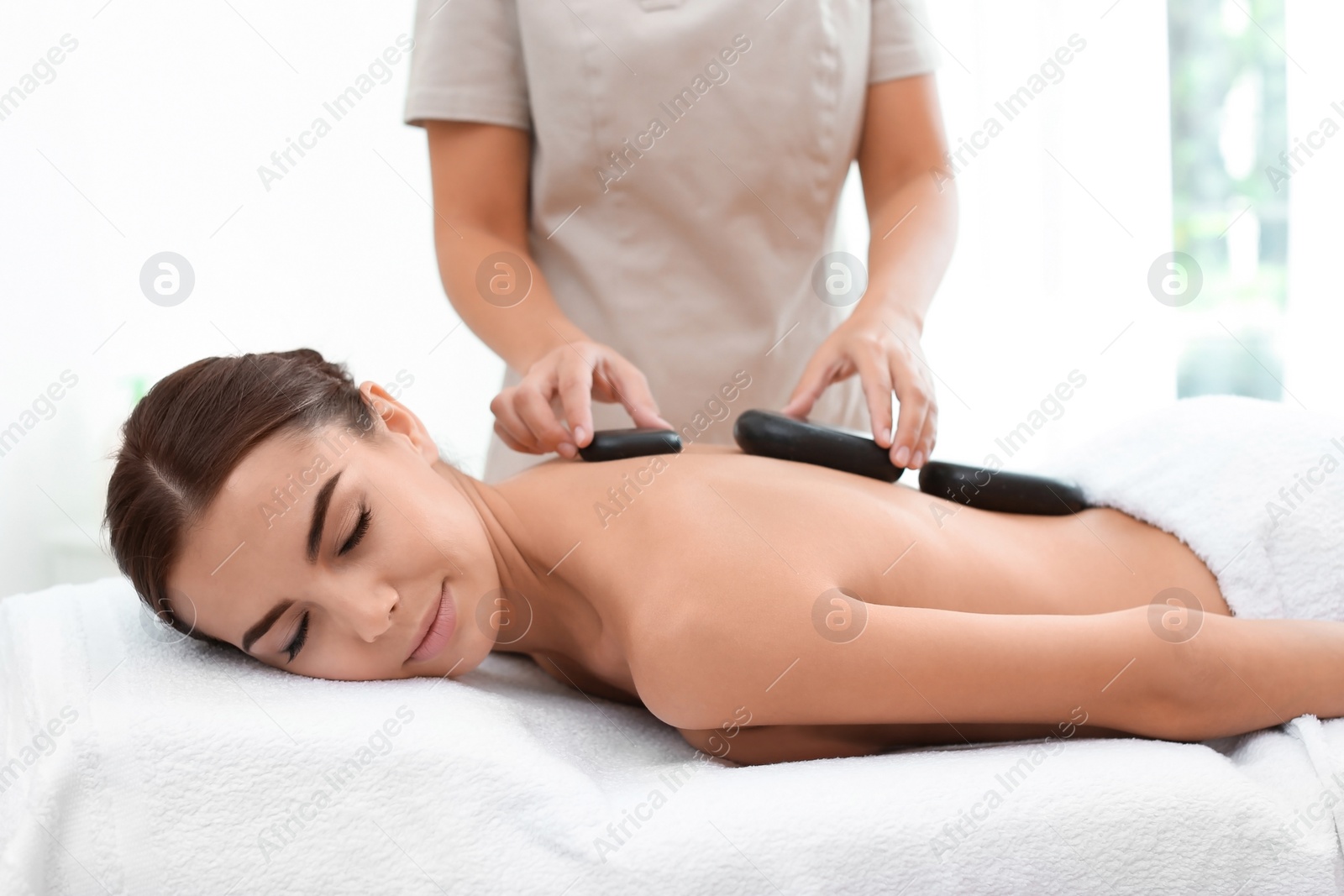 Photo of Beautiful young woman getting hot stone massage in spa salon