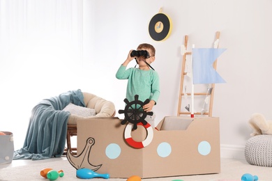 Photo of Cute little boy playing with cardboard ship at home