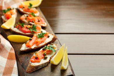 Photo of Tasty canapes with salmon, capers, lemon and cream cheese on wooden table, closeup. Space for text