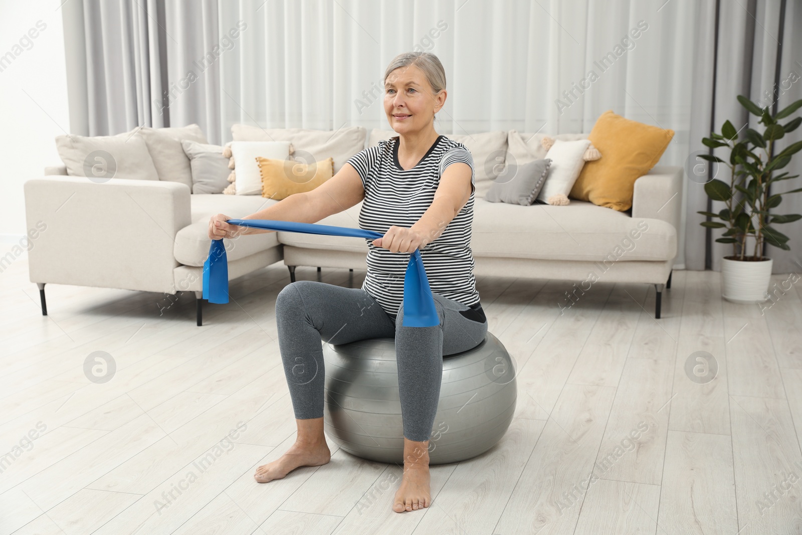 Photo of Senior woman doing exercise with elastic resistance band on fitness ball at home