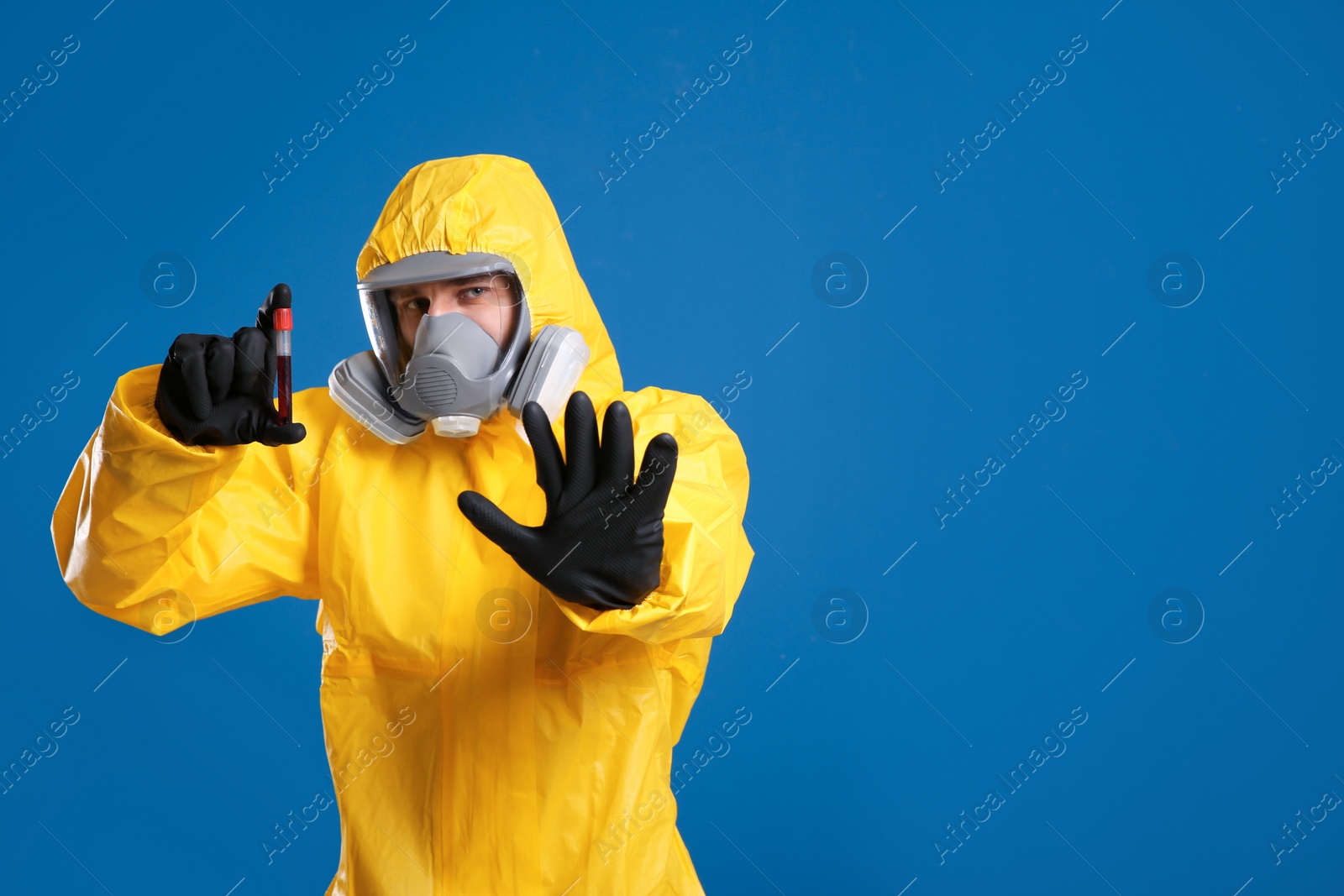 Photo of Man in chemical protective suit holding test tube of blood sample on blue background, space for text. Virus research