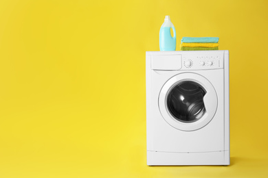 Photo of Modern washing machine with stack of towels and detergent on yellow background, space for text. Laundry day