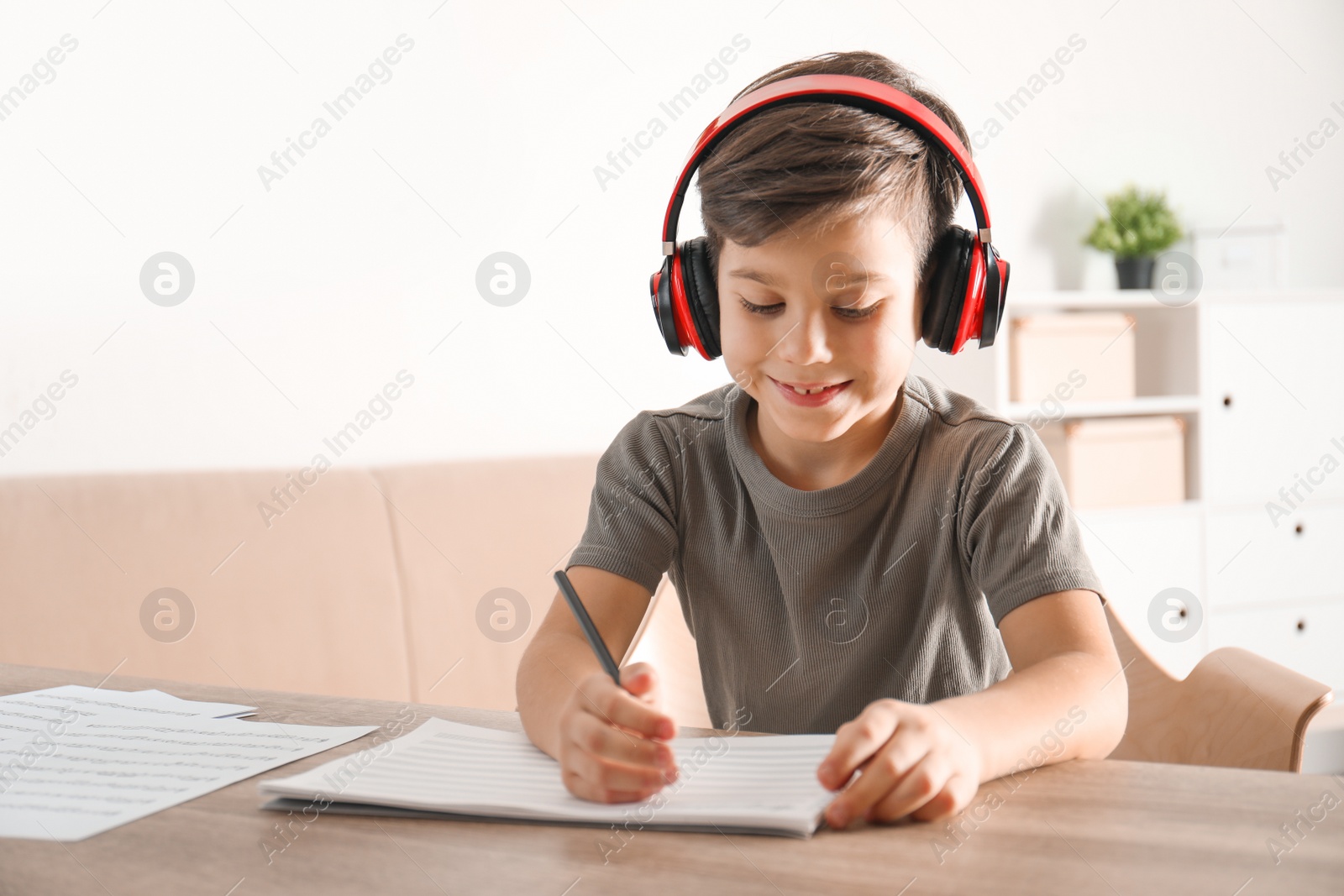 Photo of Little boy writing music notes at table indoors