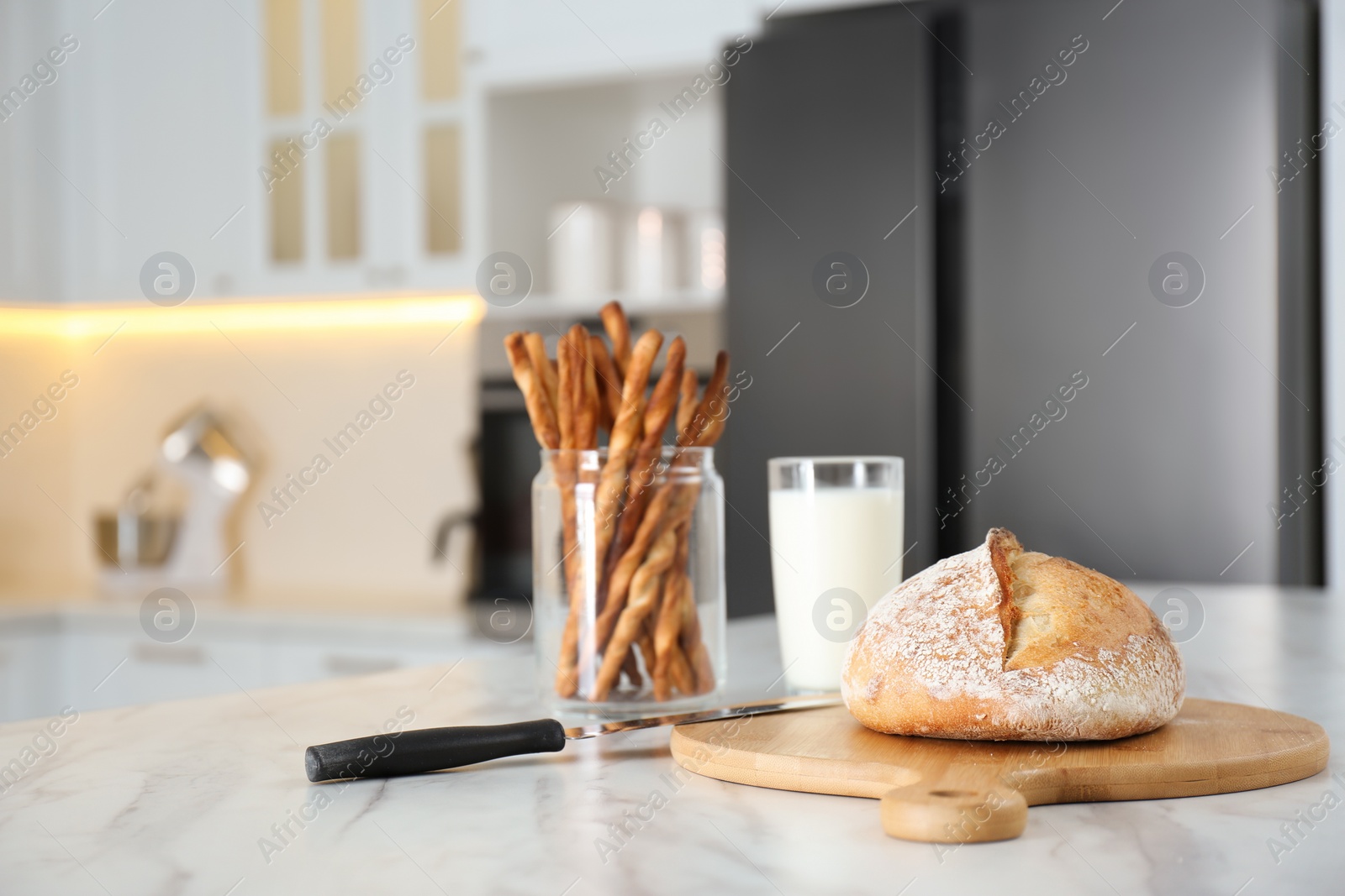 Photo of Loaf of bread and knife on white table in kitchen. Space for text