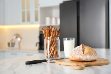Photo of Loaf of bread and knife on white table in kitchen. Space for text