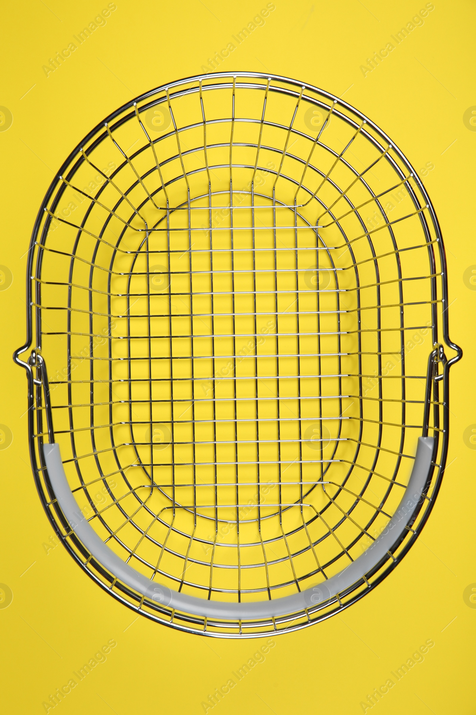 Photo of Empty metal shopping basket on yellow background, top view