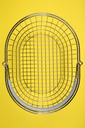 Empty metal shopping basket on yellow background, top view