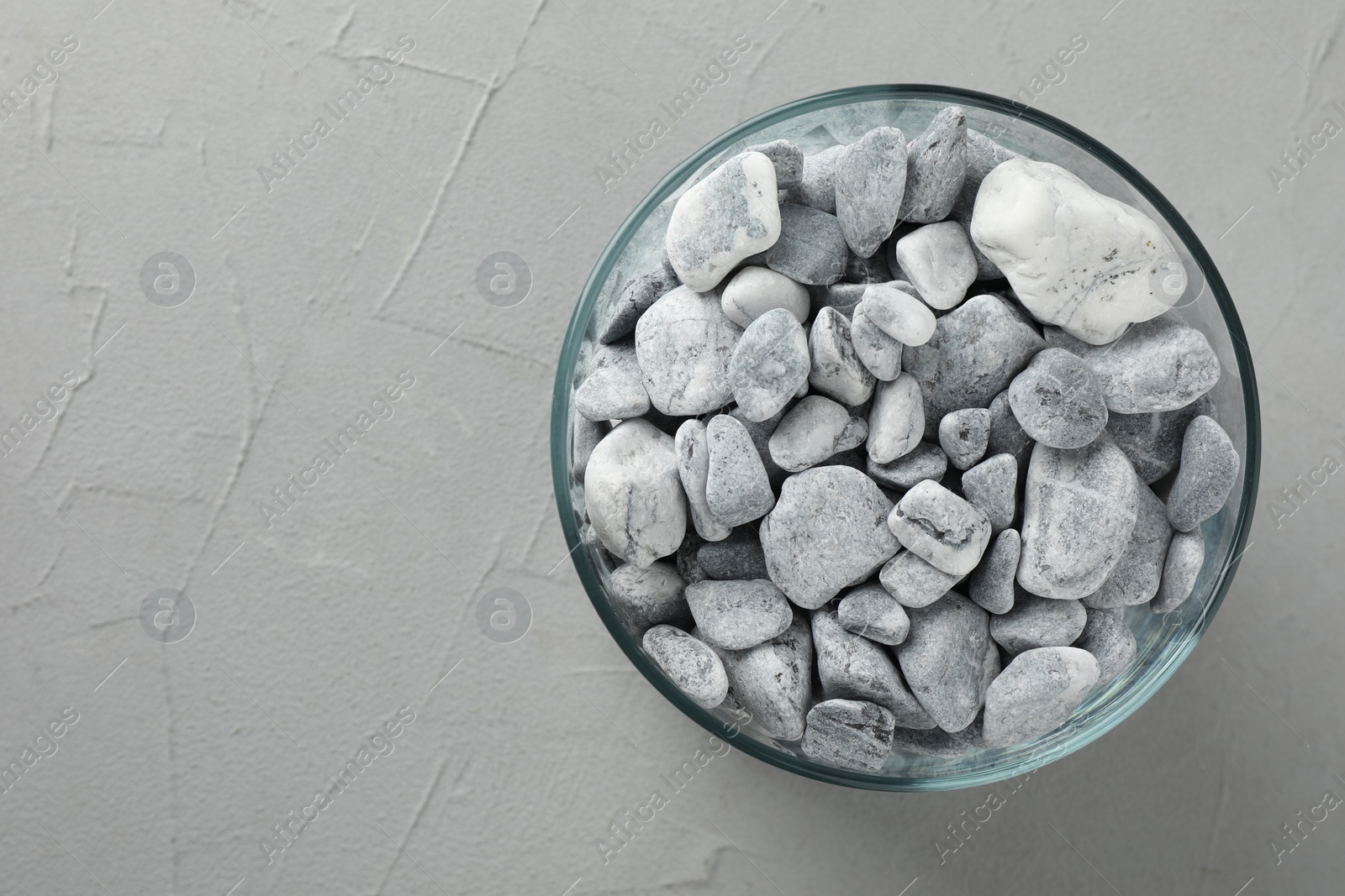 Photo of Presentation for product. Glass container with stones on grey textured background, top view. Space for text