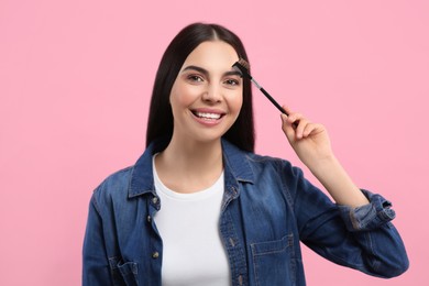 Happy woman with makeup eyebrow brush on pink background