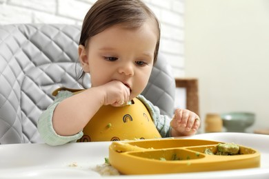 Photo of Cute little baby eating healthy food in high chair indoors