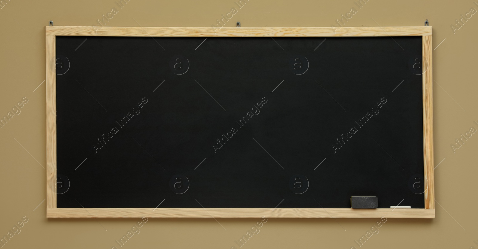 Photo of Clean black chalkboard hanging on beige wall