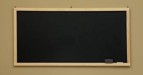 Photo of Clean black chalkboard hanging on beige wall