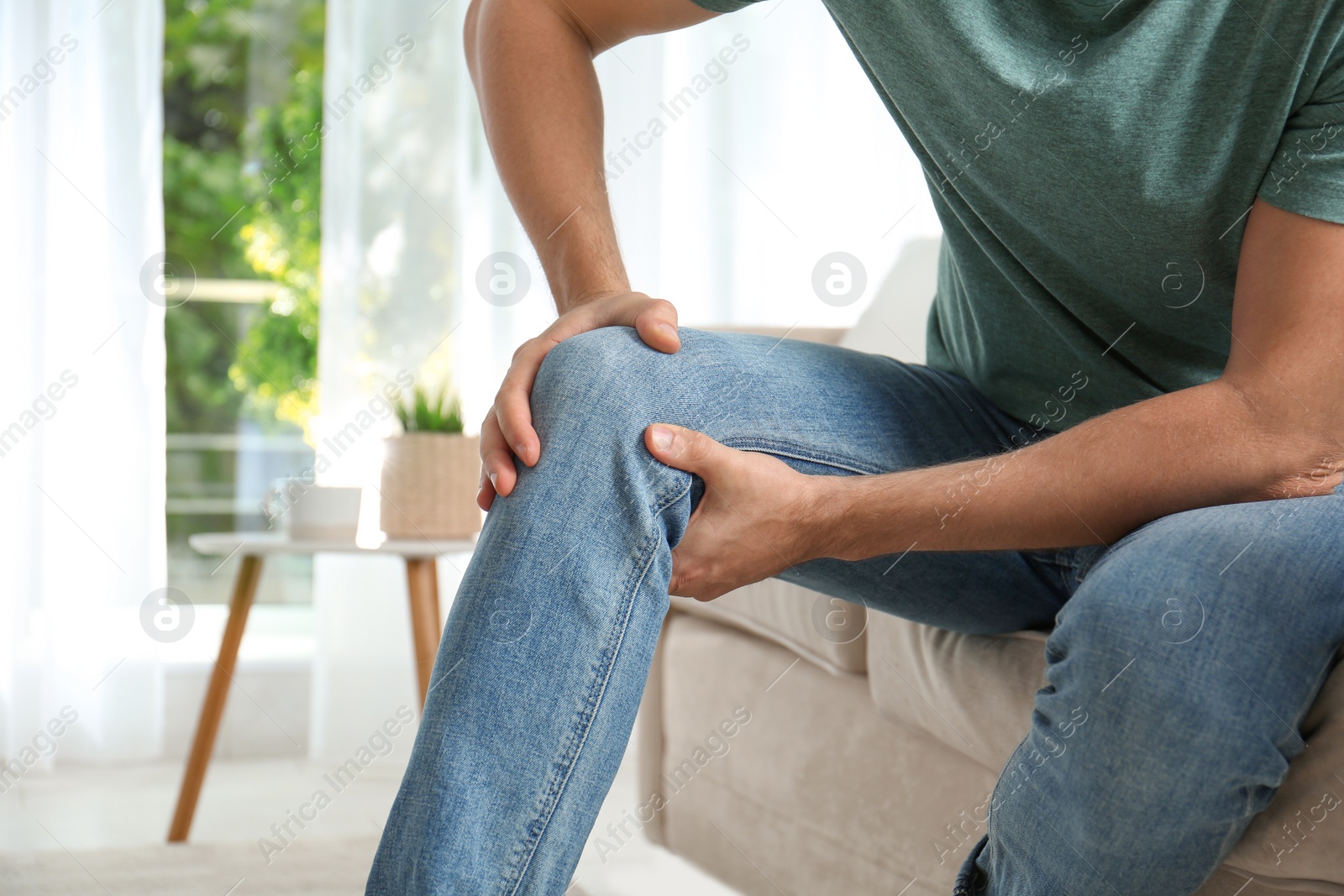 Photo of Man suffering from knee pain at home, closeup. Health problems