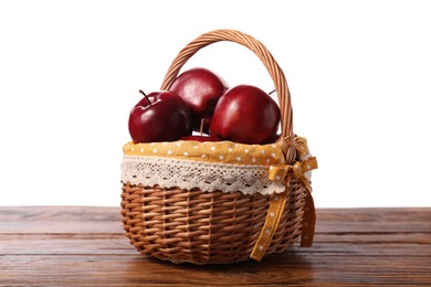 Photo of Fresh ripe red apples in wicker basket on wooden table against white background