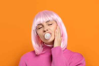 Photo of Beautiful woman blowing bubble gum on orange background