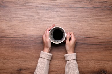 Photo of Woman with cup of coffee at wooden table, top view