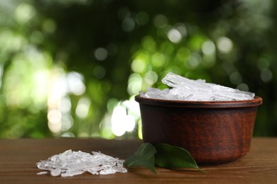 Photo of Menthol crystals and green leaves on wooden table against blurred background. Space for text