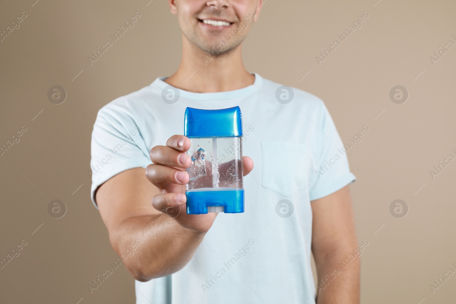 Photo of Young man holding deodorant on beige background, closeup. Mockup for design