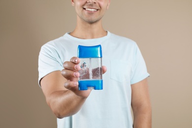 Photo of Young man holding deodorant on beige background, closeup. Mockup for design