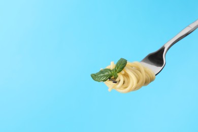 Photo of Fork with tasty pasta and basil on light blue background, space for text