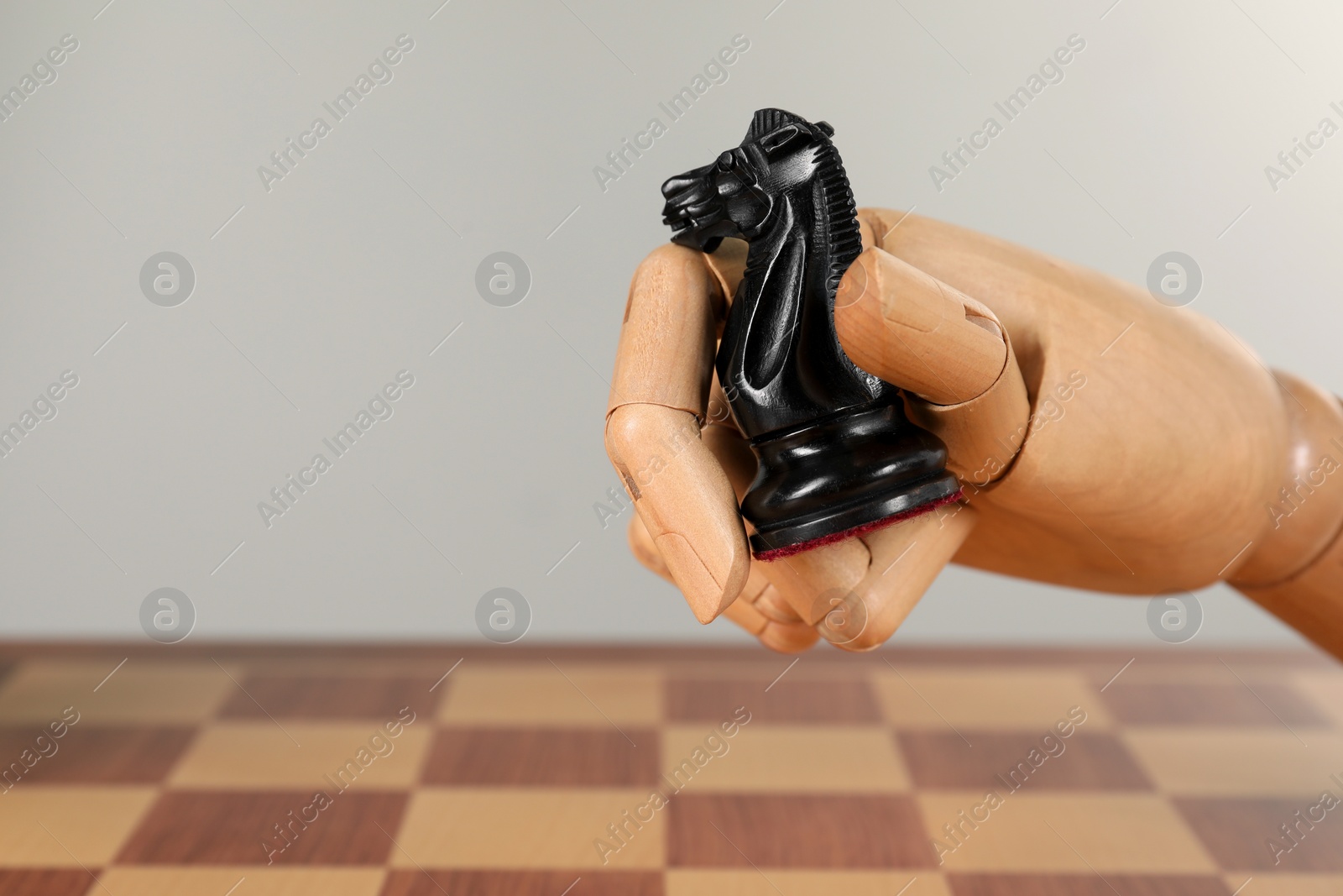 Photo of Robot with chess piece above board against light background, space for text. Wooden hand representing artificial intelligence