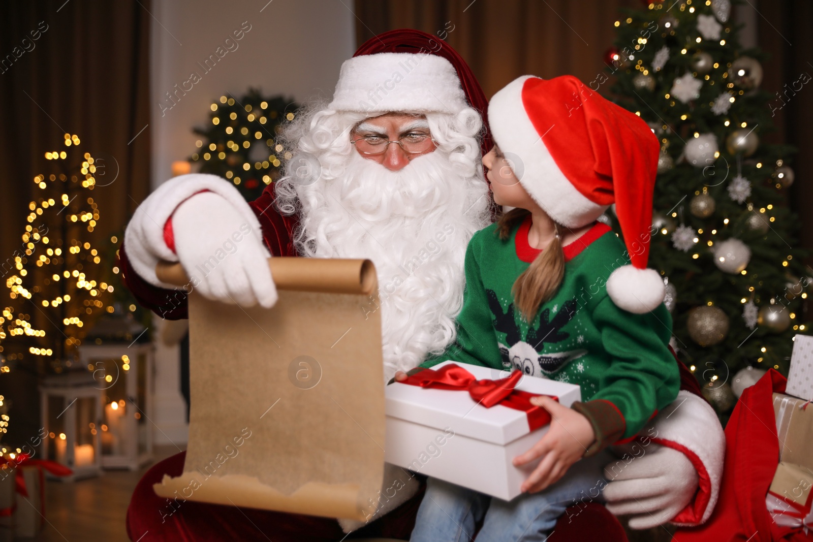 Photo of Little girl with Christmas gift near Santa Claus indoors