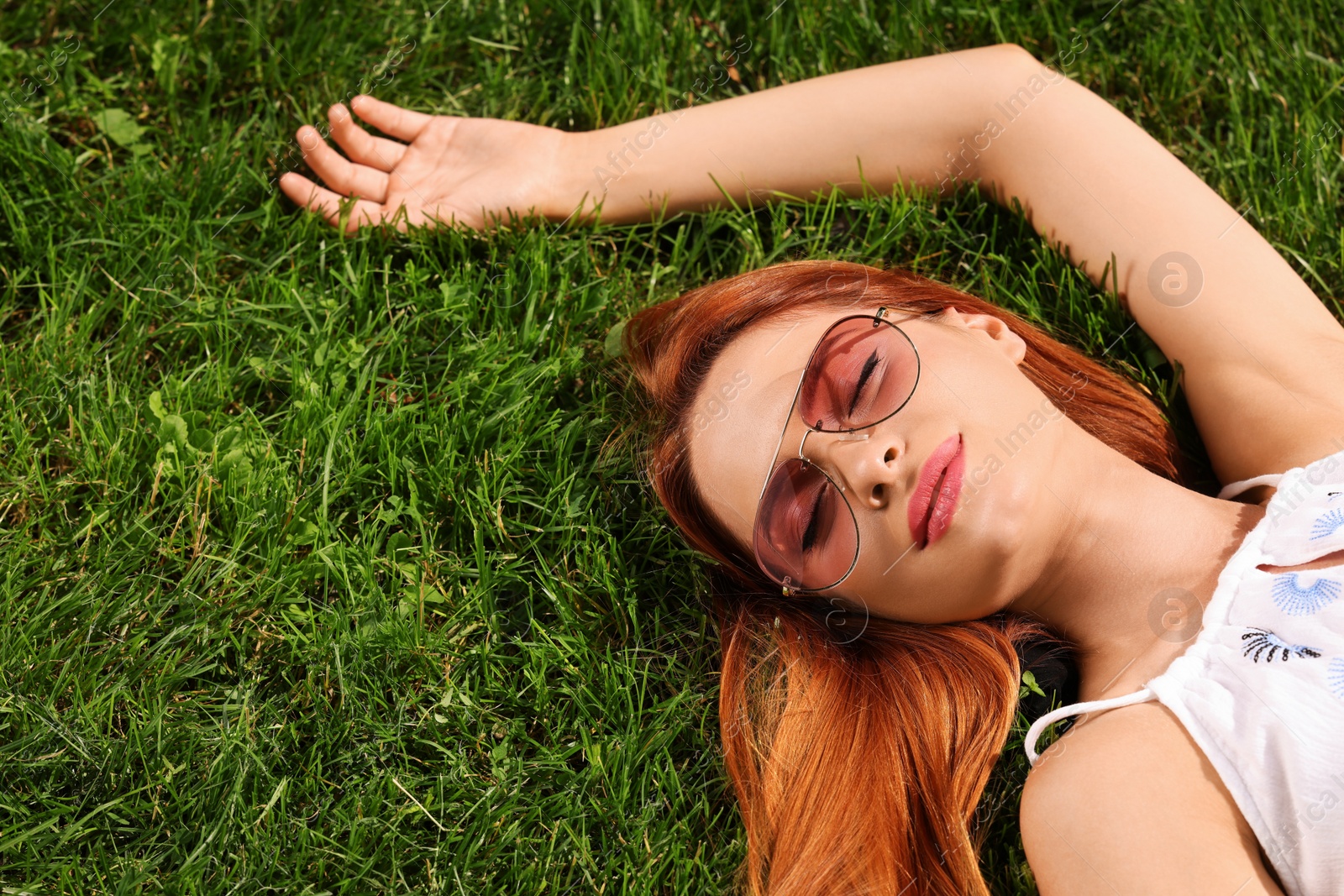Photo of Beautiful woman in sunglasses on green grass outdoors, above view. Space for text