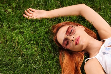 Beautiful woman in sunglasses on green grass outdoors, above view. Space for text