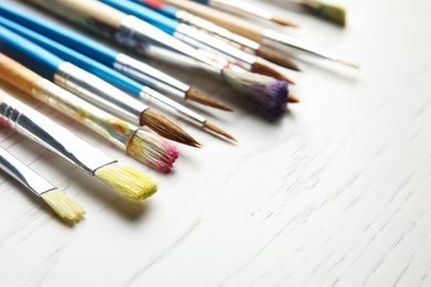 Photo of Different paint brushes on wooden table, closeup. Space for text