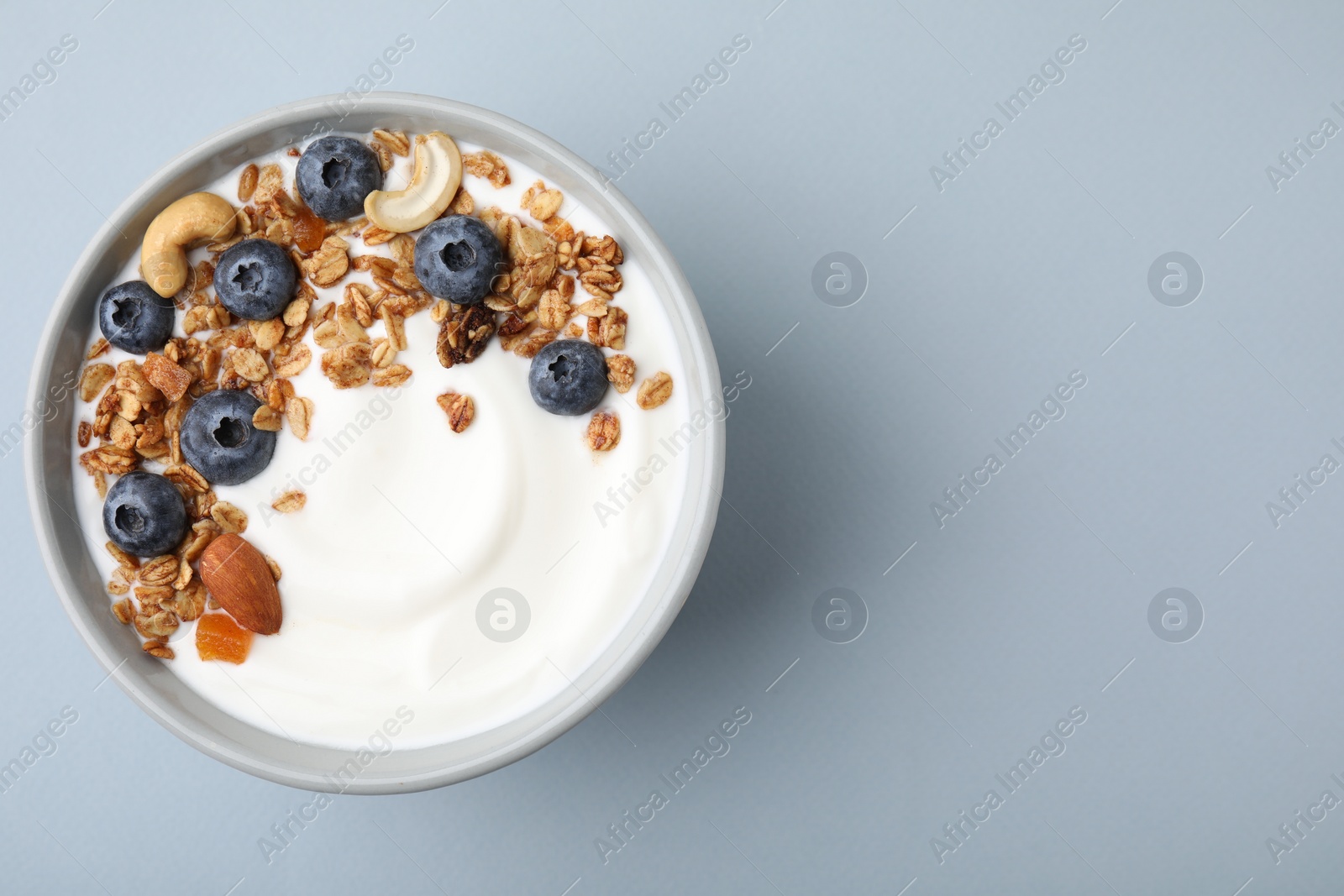 Photo of Bowl with yogurt, blueberries and granola on light grey background, top view. Space for text