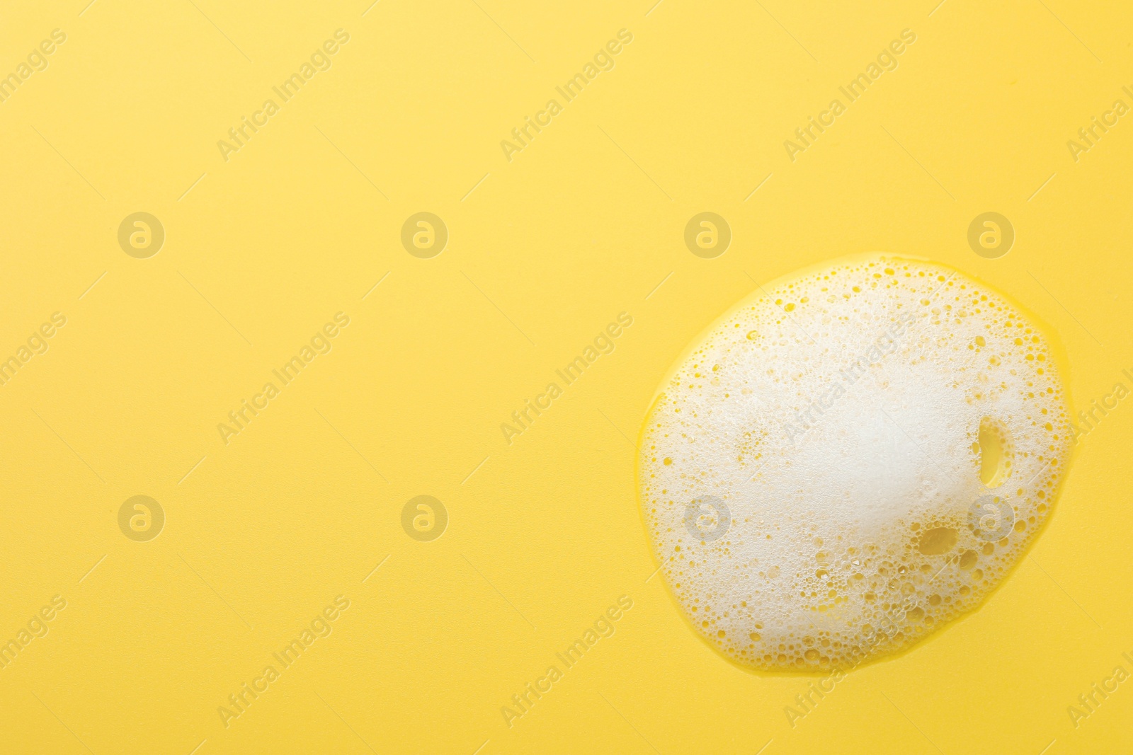 Photo of Fluffy soap foam on yellow background, top view. Space for text